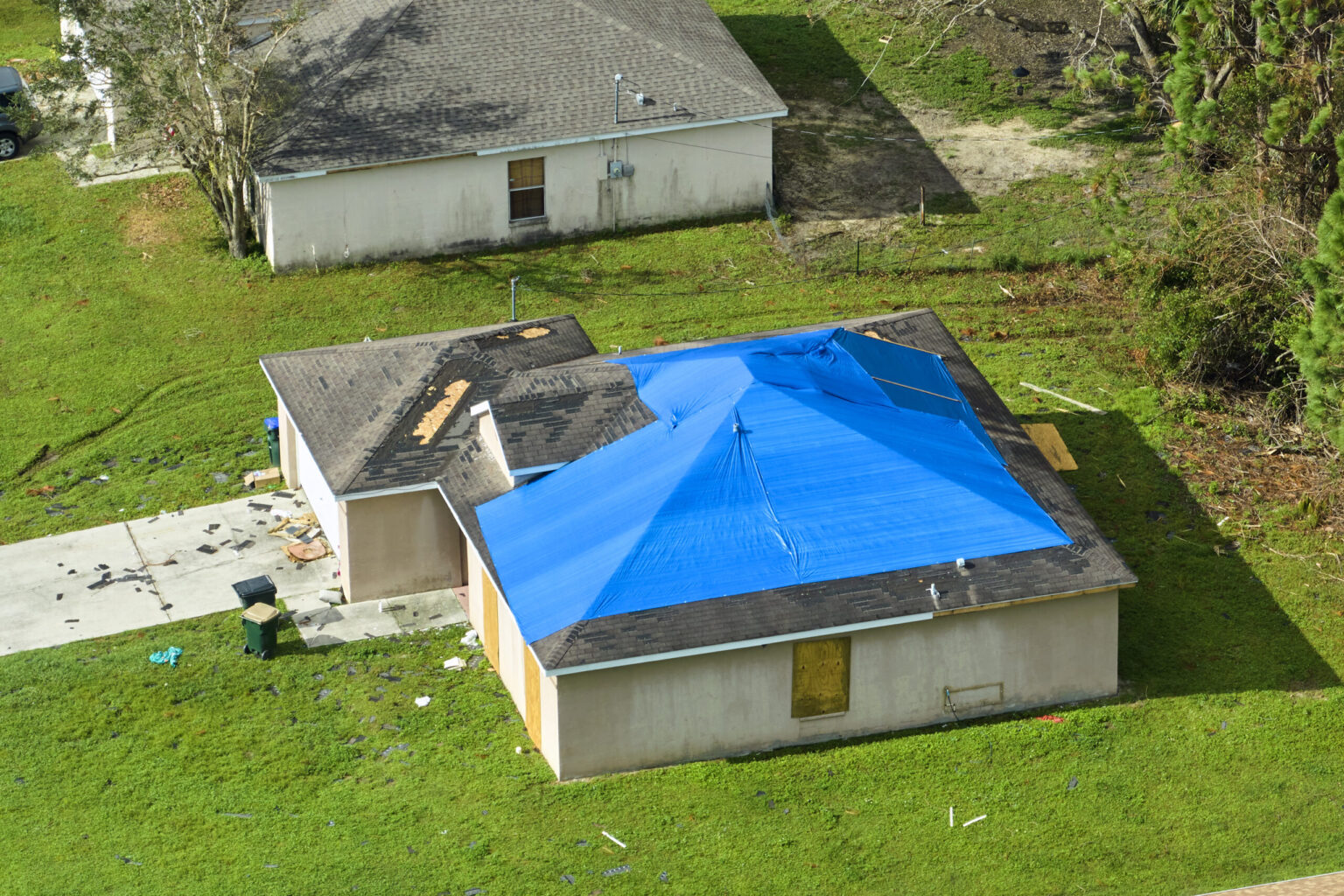 After the Storm: How Alpha Exteriors and Construction Restores Peace of Mind One Home at a Time Top view of leaking house roof covered with protective tarp sheets against rain water leaks until replacement of asphalt shingles. Damage of building rooftop as aftermath of hurricane Ian in Florida